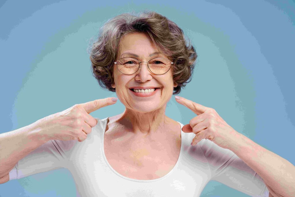 A woman with glasses dressed in a white shirt is using her fingers to point, highlighting her dental implants.