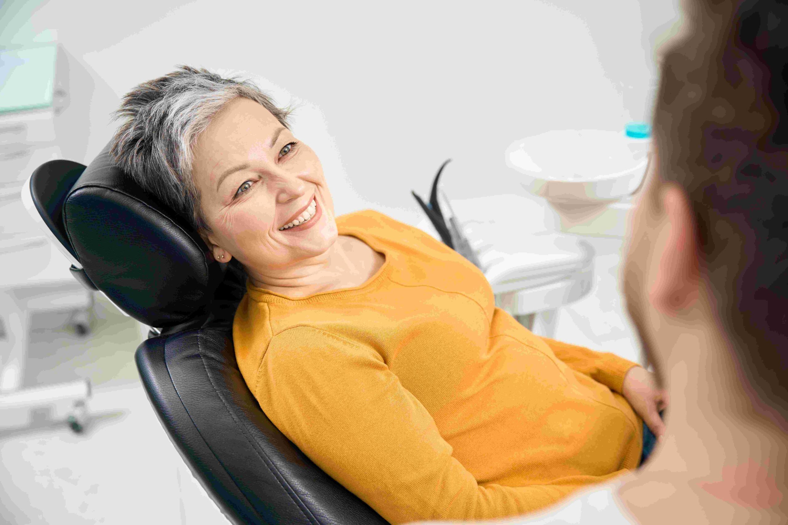 A woman in a dental chair, with a man beside her, both looking attentive as they discuss her dental care.